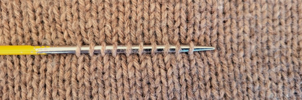 Aiguille à tricoter glissée dans les mailles d'un tricot